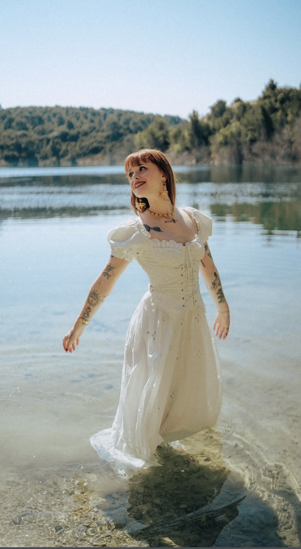 Ivy en robe blanche dans l'eau devant un lac